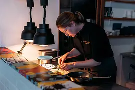Eine Köchin richtet in einer Restaurantküche unter warmem Licht sorgfältig ein Gericht an.