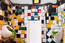 Artistic public toilet with colorful mosaic tiles and organic forms inspired by Hundertwasser’s architectural style.