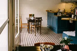 Small restaurant with wooden tables, patterned tile floor and open kitchen.