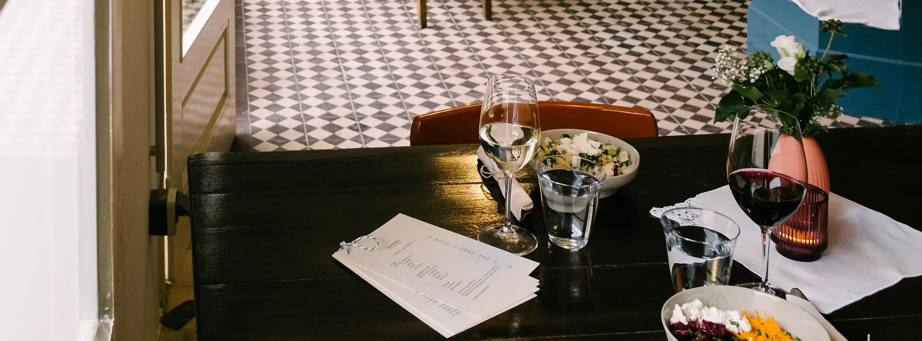 Small restaurant with wooden tables, patterned tile floor and open kitchen.