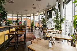 Bright rooftop venue with large windows, lush plants and city views.