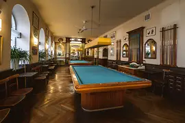 Historic billiards room with two tables, wood paneling and cue racks.