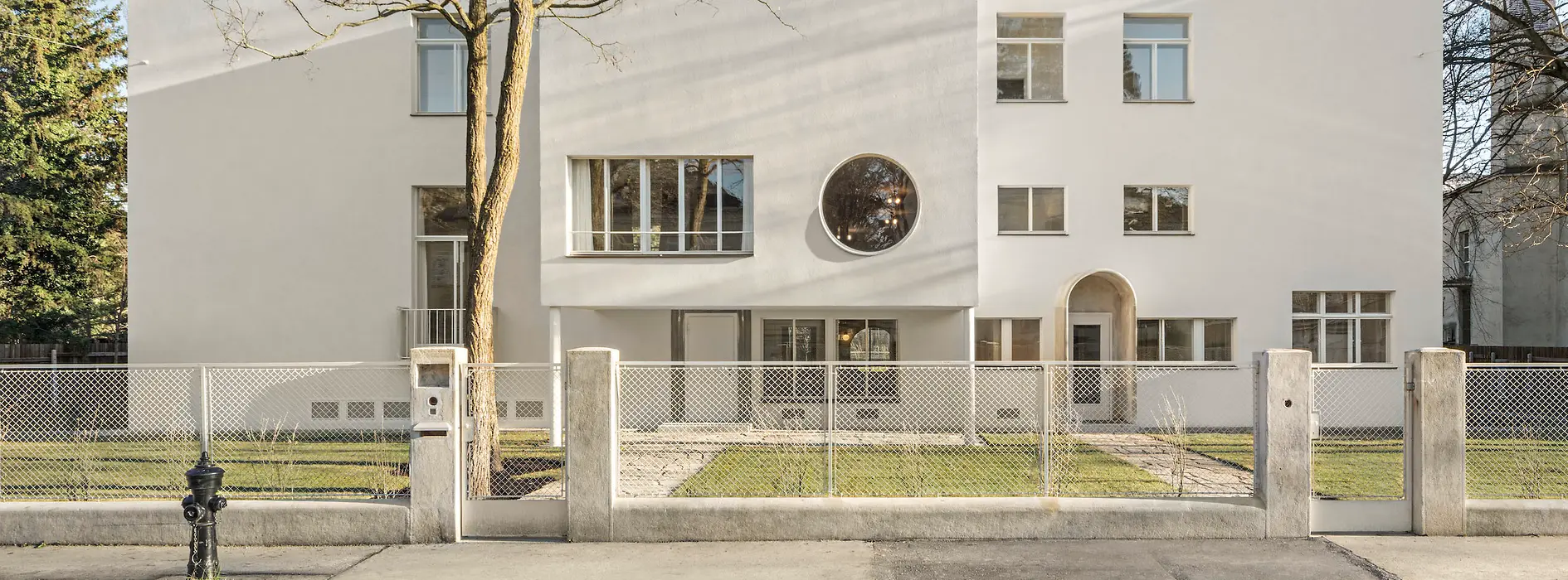 Street view of the modernist villa with circular window and recessed entrance.