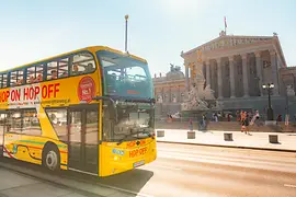 Yellow hop-on hop-off double-decker bus by Vienna Sightseeing Tours in front of the Parliament