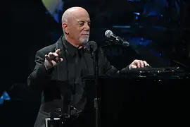 Billy Joel am Klavier lehnend, vor sich das Mikrofon.
