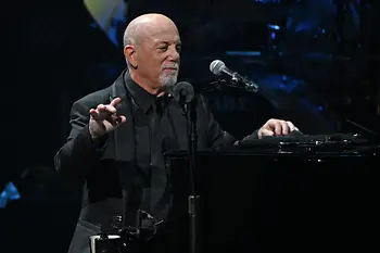 Billy Joel leaning on the piano, the microphone in front of him.