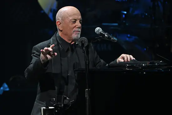 Billy Joel leaning on the piano, the microphone in front of him.