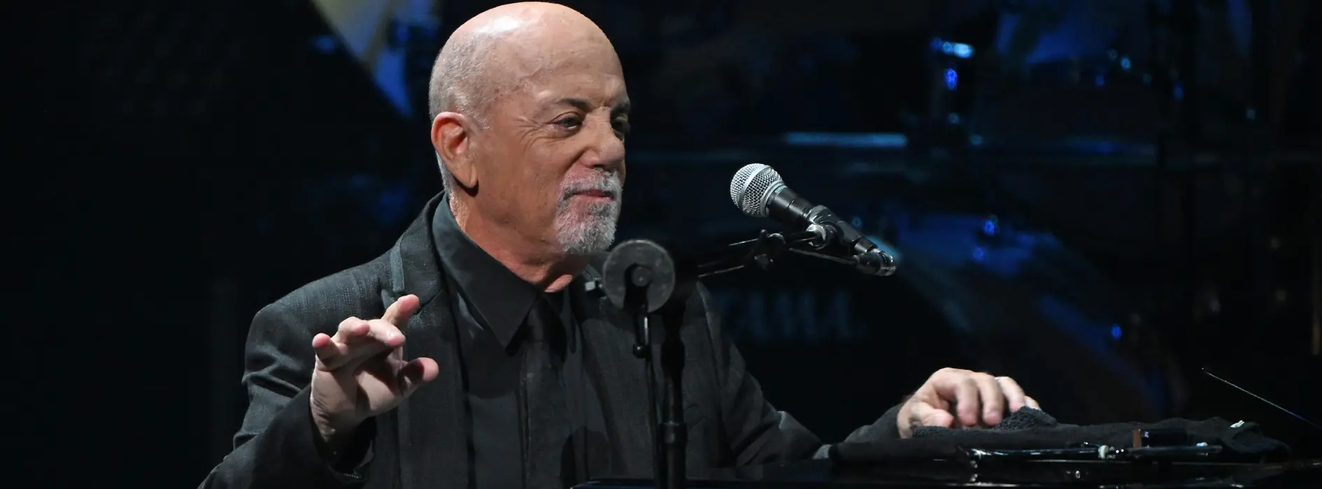 Billy Joel am Klavier lehnend, vor sich das Mikrofon.