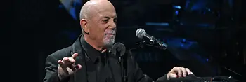 Billy Joel leaning on the piano, the microphone in front of him.