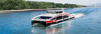 The high-speed catamaran Twin City Liner sails on the Danube with alluvial forest in the background.