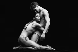 Two ballet dancers kneeling on the floor and embracing each other closely