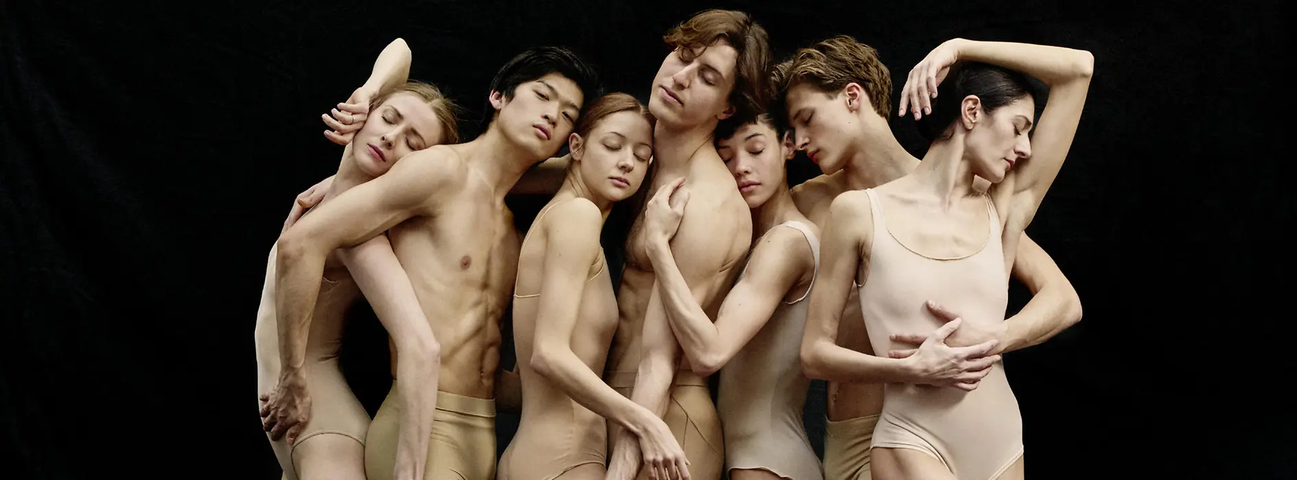 Seven ballet dancers standing close together in pose.