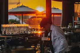 Hote Motto Rooftop bar Chez Bernard, bartender mixing drinks, sunset in the background