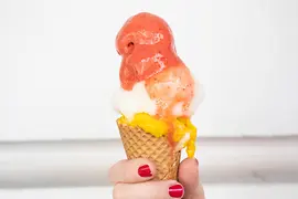 Main aux ongles peints en rouge tenant un cornet de glace avec trois boules, photographié à Vienne
